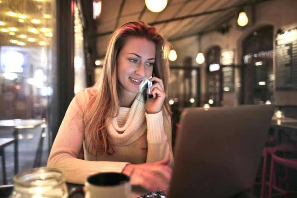 a woman talking on her phone and using her laptop at a coffee shop